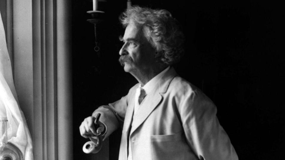 Mark Twain looks out a window while holding a smoking pipe