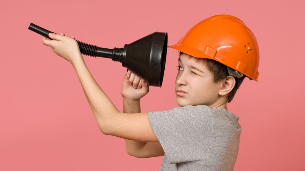 A boy in a hard hat peers into the wide end of a funnel, which he is holding like a telescope.