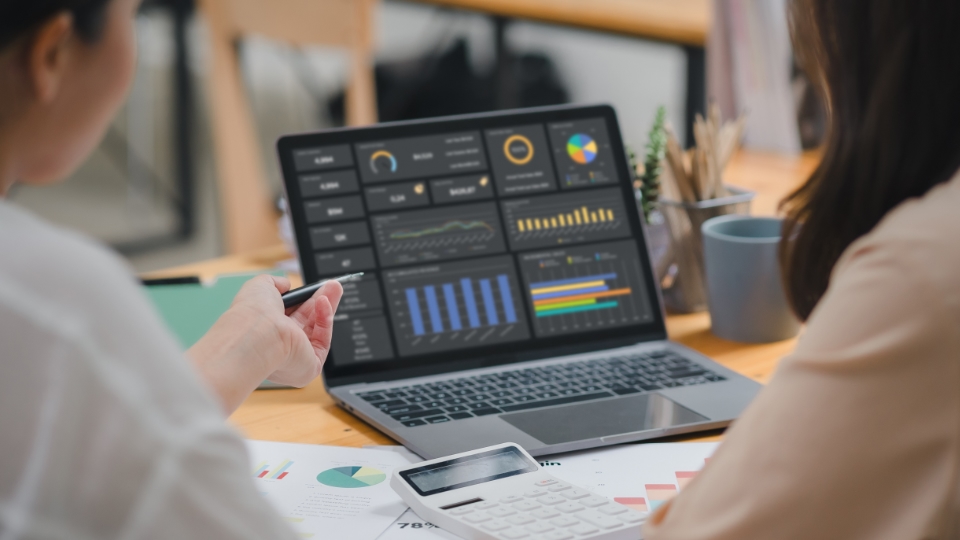 Two people look at a laptop displaying metrics on the screen