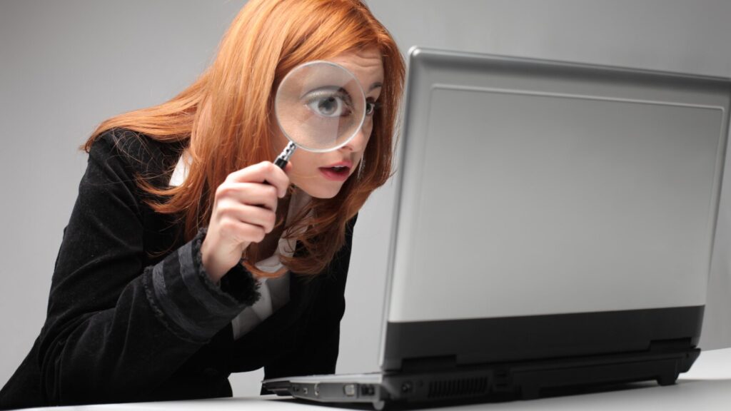 Woman examining laptop with a magnifying glass