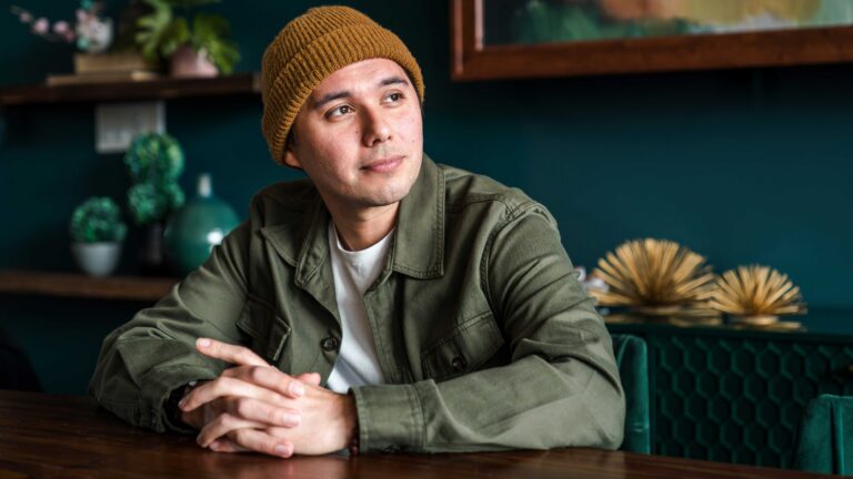 man smiling softly while sitting with his hands folded at a table