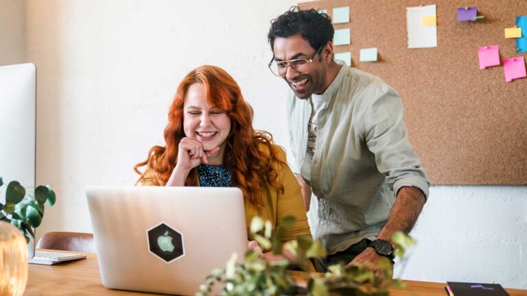 Smiling colleagues look at a laptop.