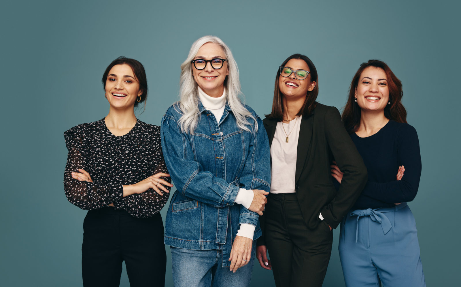 Multicultural group of women smiling at the camera with confidence. Four women of different ages standing together against a studio background. Strong independent women embracing empowerment.