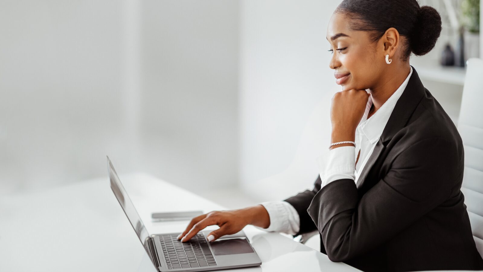 A woman in a business suit looks thoughtfully at her laptop screen.